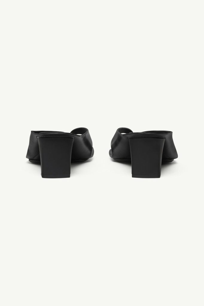 Pair of black heeled mules seen from behind, featuring chunky square heels and open backs.