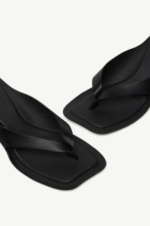 Black leather thong sandals with a square toe and crisscross straps on a light background