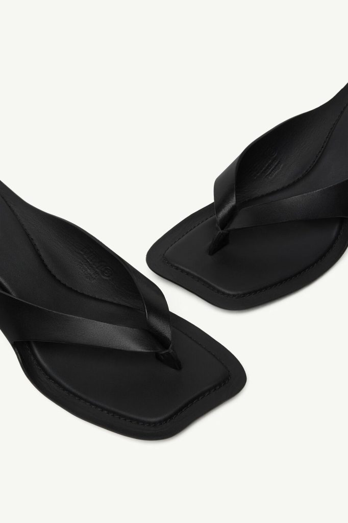 Black leather thong sandals with a square toe and crisscross straps on a light background