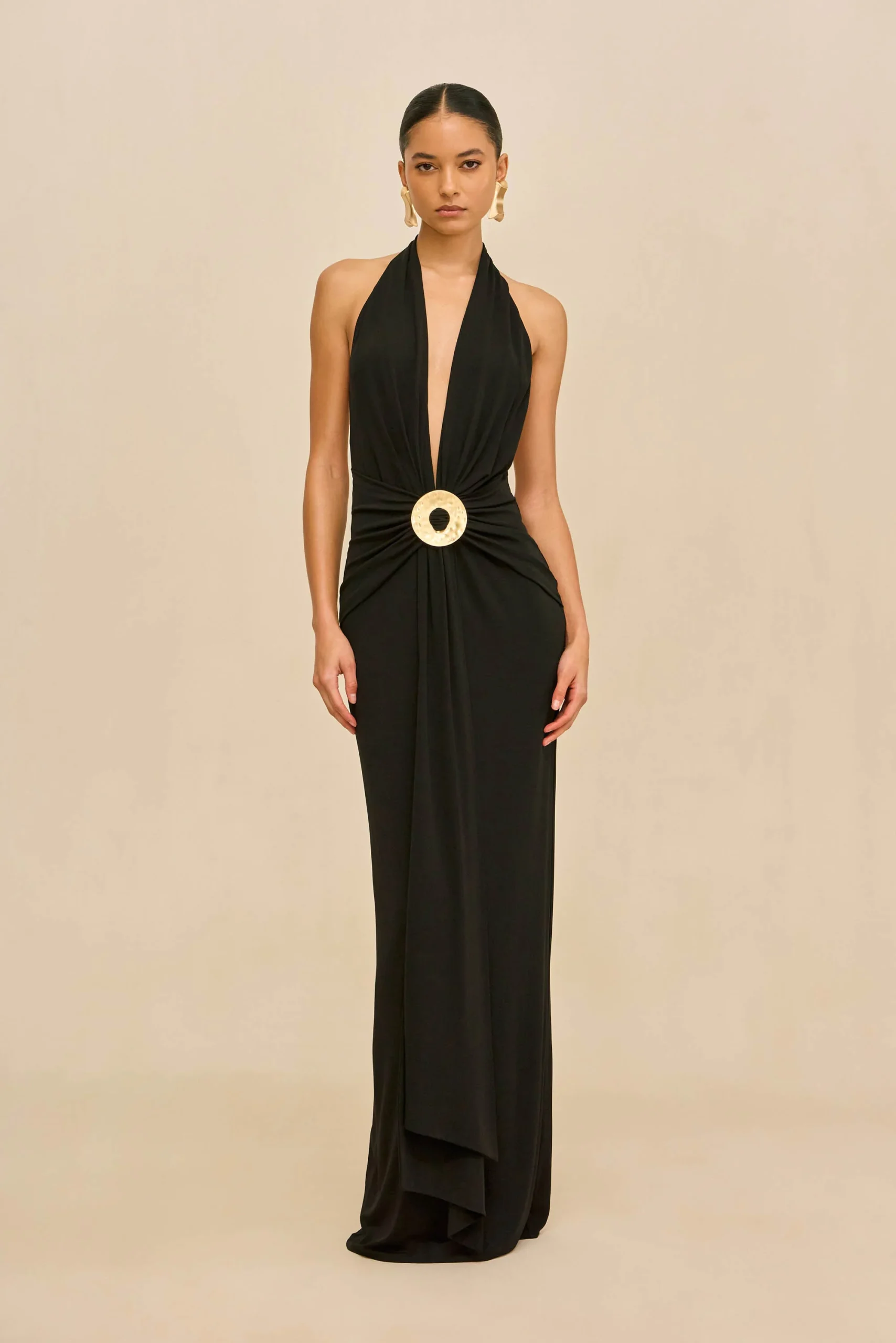 IMG_1275 - New Trend Model in a long black halter gown with a large gold circular belt buckle, standing against a beige backdrop.