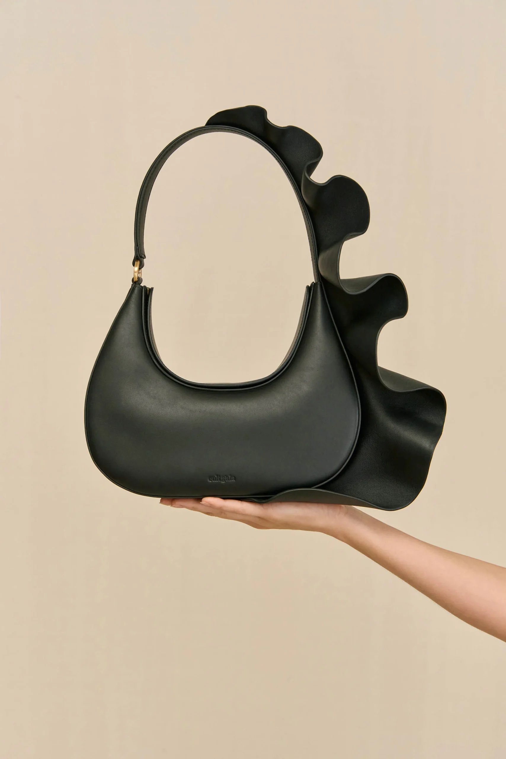 IMG_1282 - New Trend Black handbag with a large sculptural ruffle along the side, held by a hand.