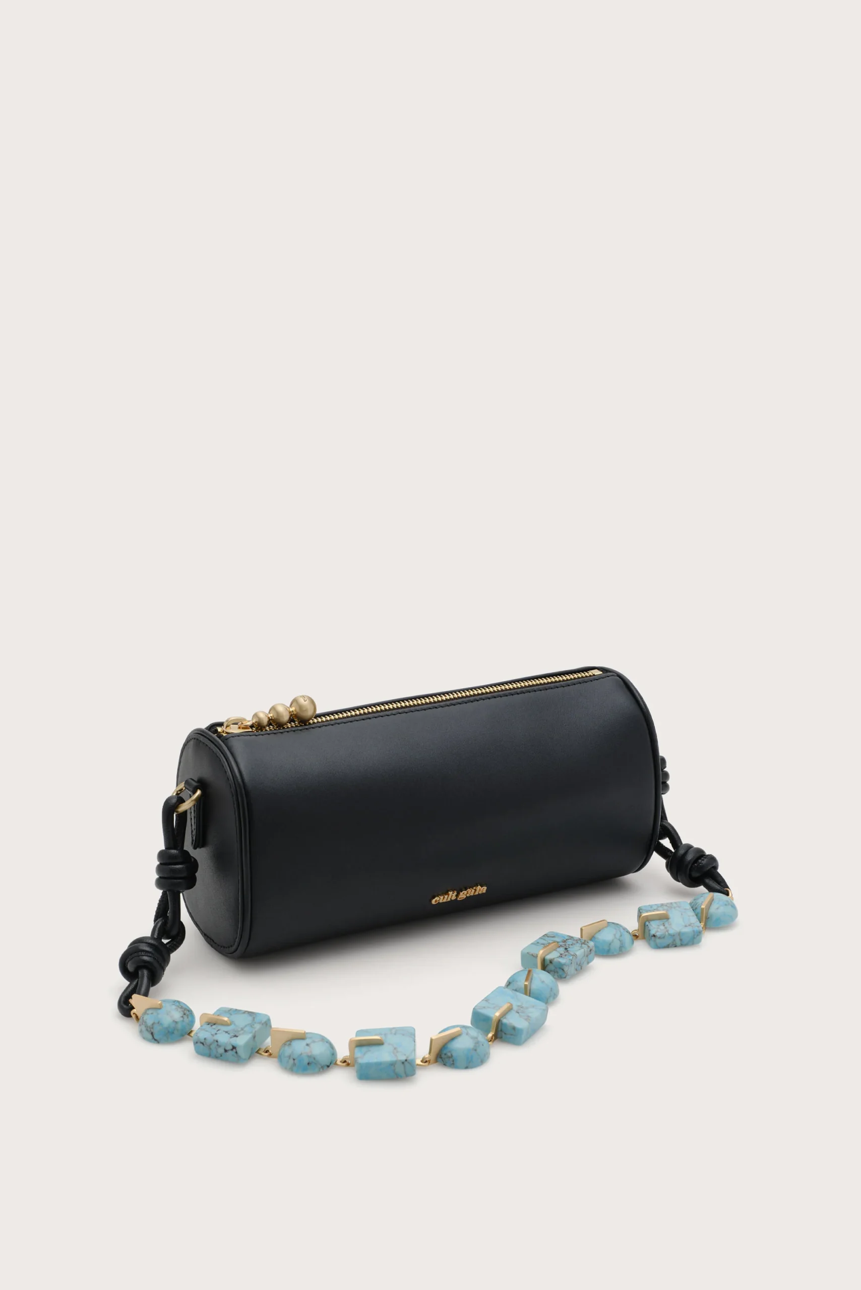 IMG_1291 - New Trend Black cylindrical handbag with a gold zipper, placed on a light background, with a turquoise bead necklace in front.