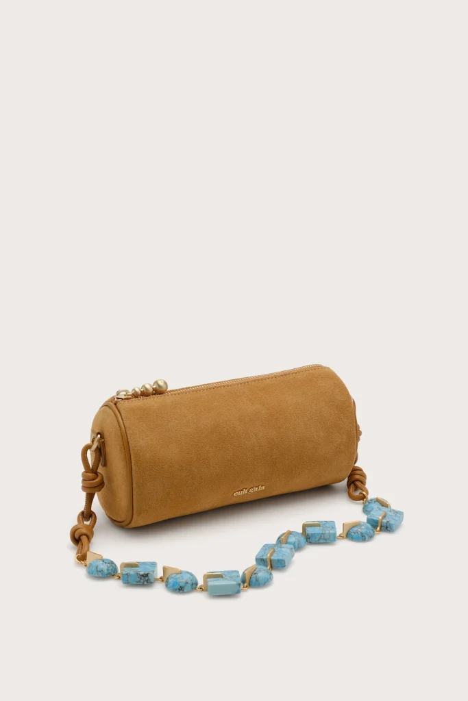 Tan suede crossbody bag with gold zipper and chain strap, shown with turquoise beaded necklace nearby.