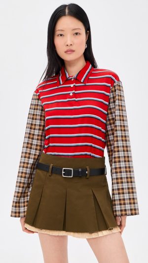 Woman wearing a red striped polo shirt with plaid sleeves and a brown pleated mini skirt with a black belt.
