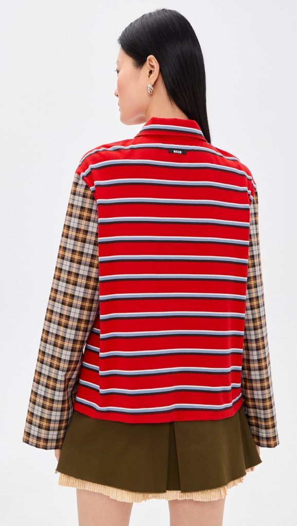 Back view of person wearing a red striped vest over a plaid long-sleeve shirt and an olive skirt with fringe hem.