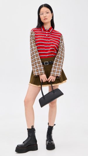 Model in a red striped polo with plaid sleeves, olive mini skirt, black belt, and chunky black boots, holding a small black handbag.