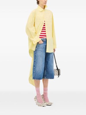 Person in a pale yellow oversized coat over a red-and-white striped top, wide denim culottes, red striped socks, spotted shoes, and a small patterned handbag.