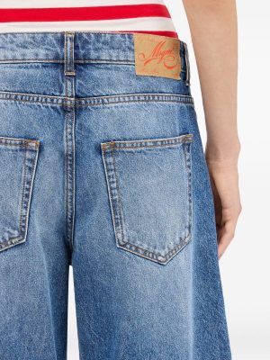 Back view of a person wearing blue denim jeans with two back pockets and a leather brand patch on the waistband; a red-and-white striped top edge is visible.