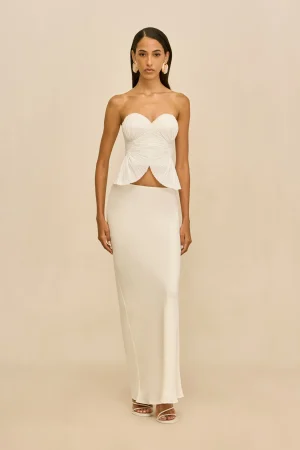 Full-length view: model in a white strapless dress with ruched bodice and peplum, standing against a beige backdrop.