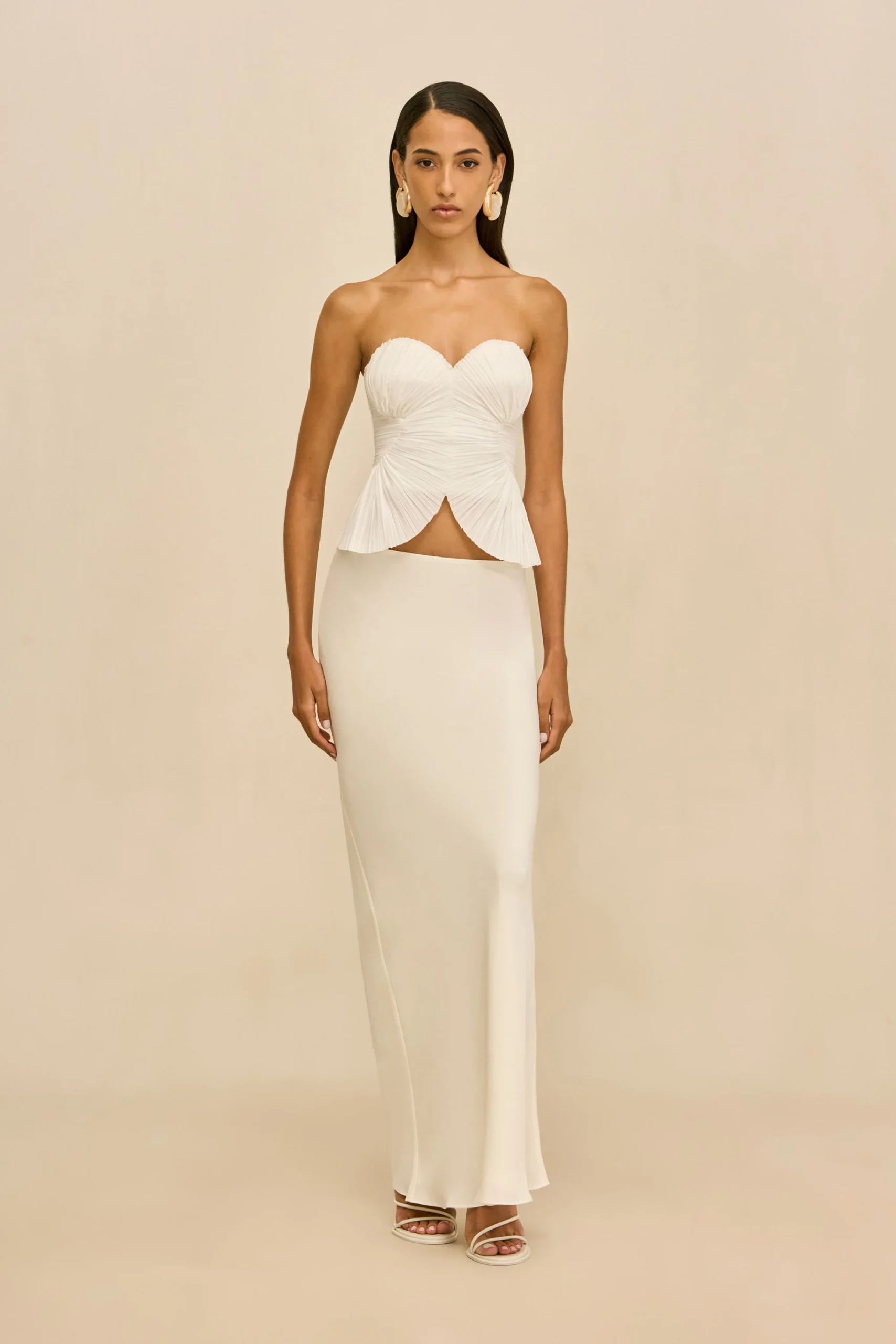 IMG_1381 - New Trend Full-length view: model in a white strapless dress with ruched bodice and peplum, standing against a beige backdrop.