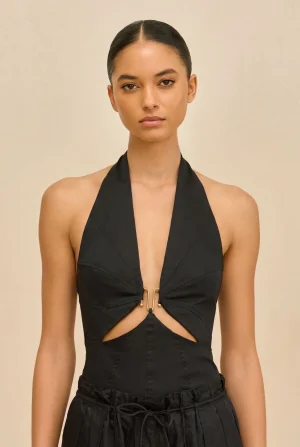Model wearing a black halter top with a front knot and gold hardware against a beige backdrop, posed for a fashion shoot jaw-length portrait.