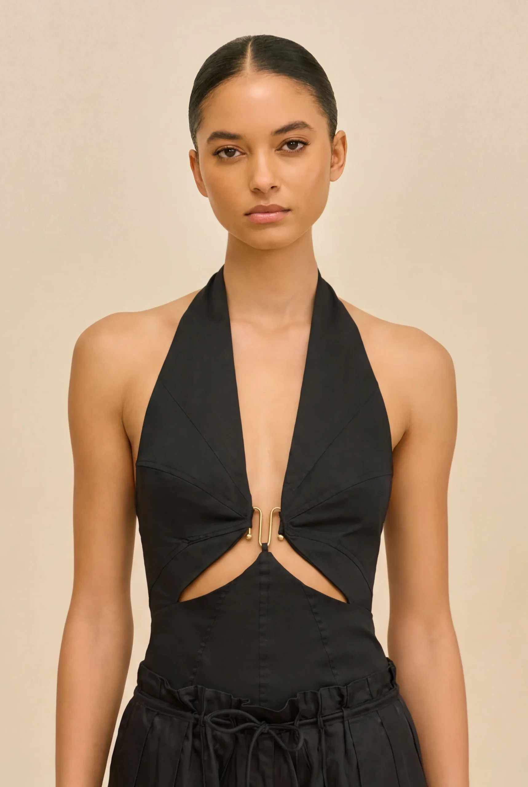 IMG_1384 - New Trend Model wearing a black halter top with a front knot and gold hardware against a beige backdrop, posed for a fashion shoot jaw-length portrait.