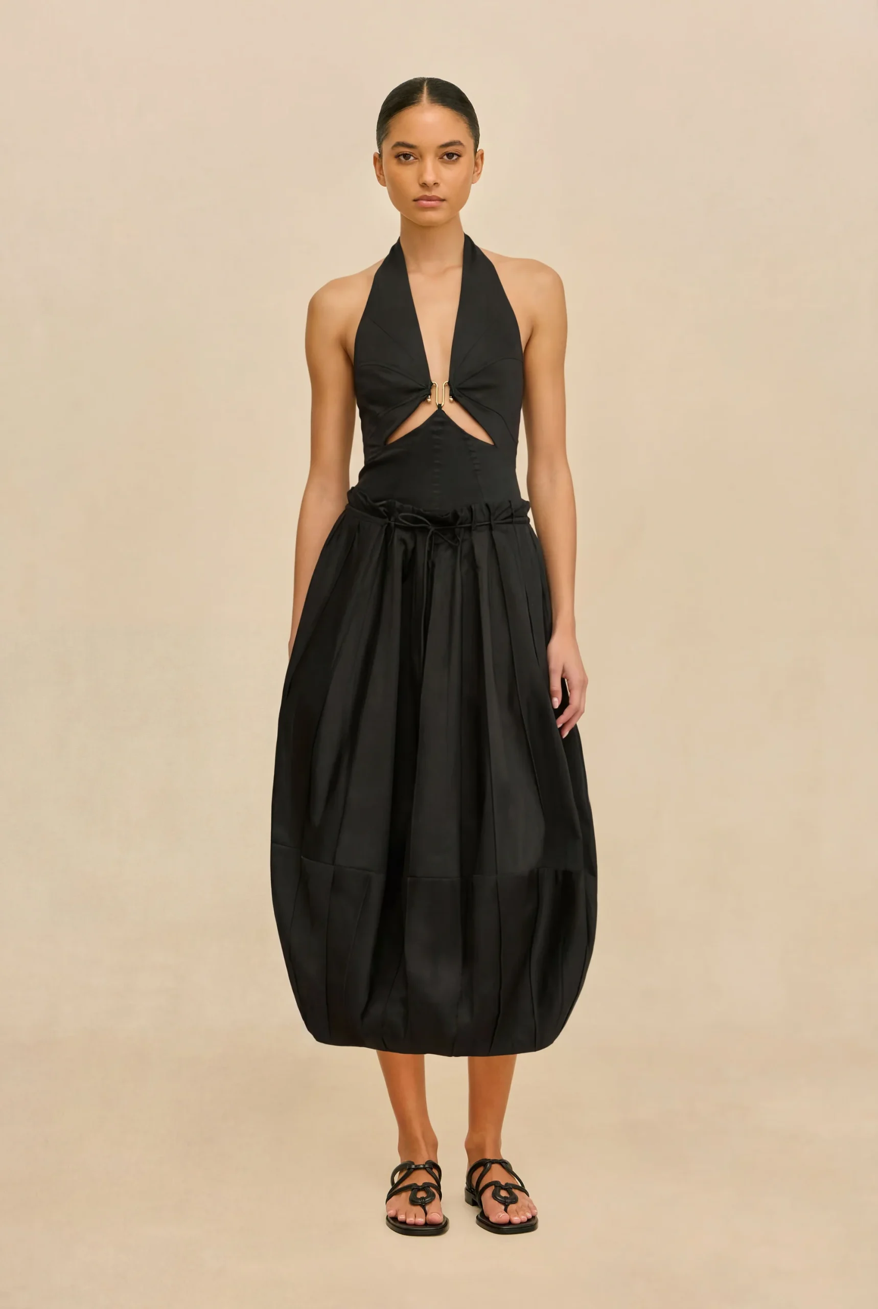 IMG_1385 - New Trend Female model wearing a black halter-neck dress with front cutouts and a voluminous midi skirt, paired with black sandals.