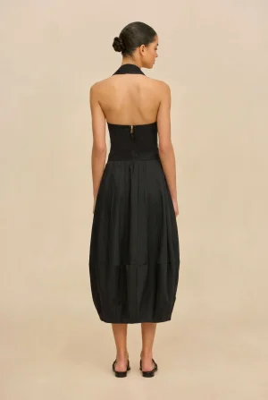 Back view of a woman in a black halter-neck dress with a center-back zipper, against a beige backdrop.