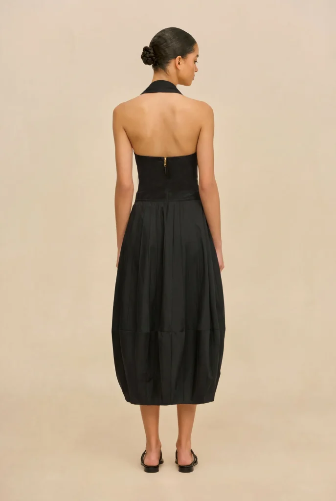 Back view of a woman in a black halter-neck dress with a center-back zipper, against a beige backdrop.