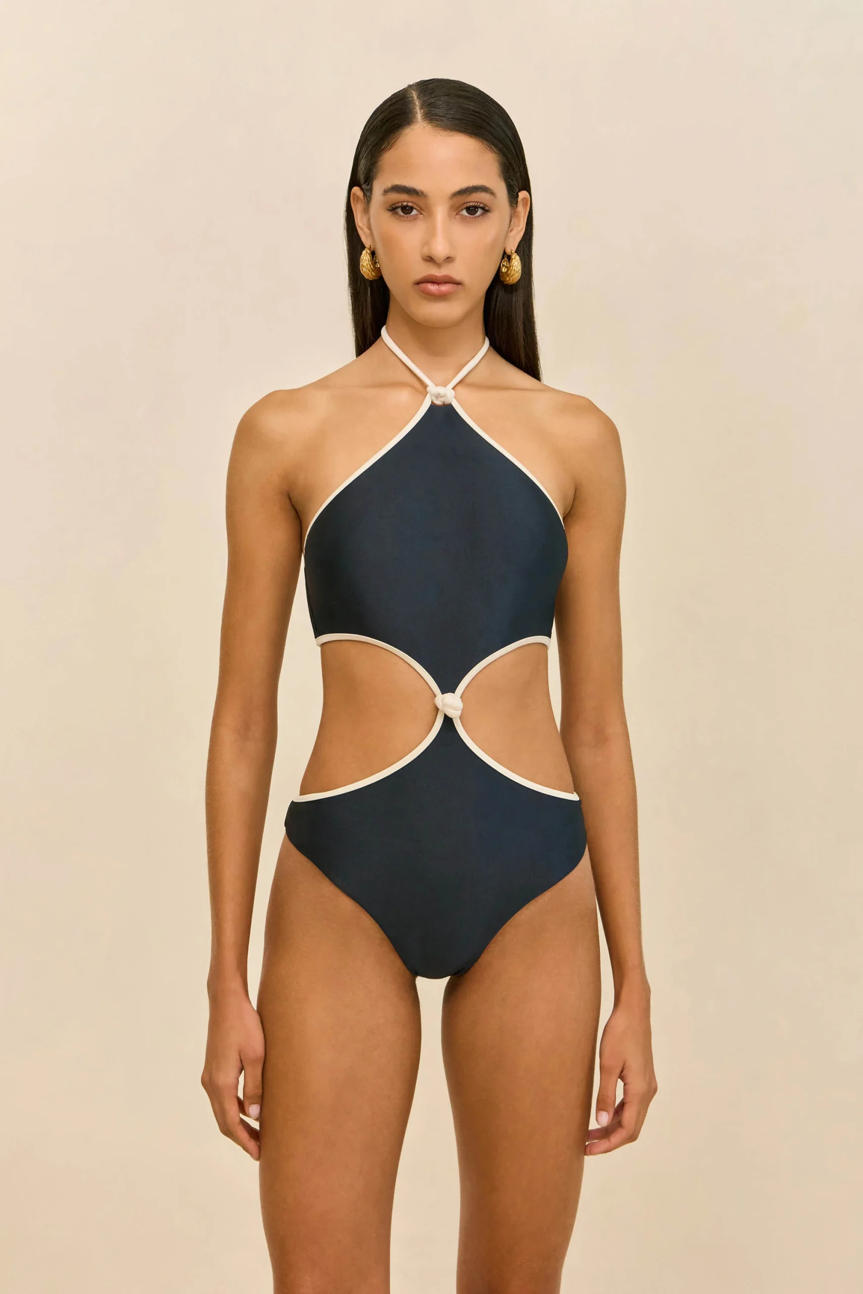 IMG_1390 - New Trend Model wearing a navy halter-neck one-piece swimsuit with white trim, standing against a beige background.