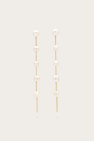 Long gold chain earrings with evenly spaced white pearls along each strand, hanging against a pale background