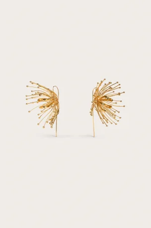 Two gold-toned wire sculpture flowers with radiating spokes, placed against a pale cream background near the bottom of the frame.