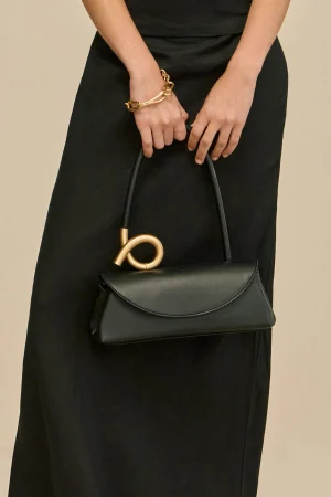 Woman in a black dress holding a small black handbag with a gold circular handle.