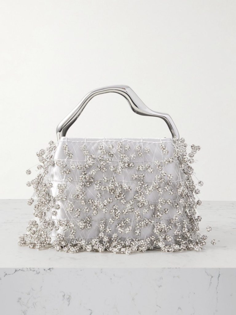 Silver clutch handbag with a sculpted metallic handle and crystal-embellished beading across white satin fabric.