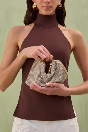 Woman in a brown halter-top holds a small, sparkling beaded clutch in front of a green background.