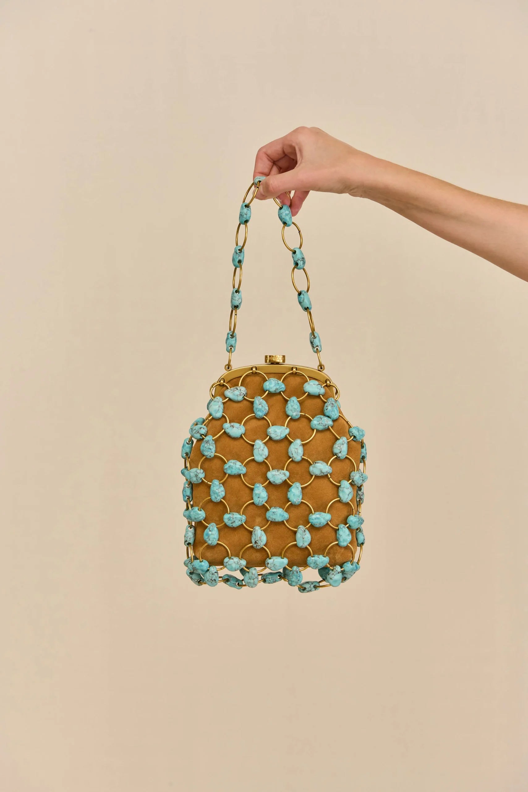 IMG_1444 - New Trend Hand holding a turquoise beaded handbag with gold links against a beige background.