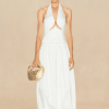 IMG_1463 - New Trend Model wearing a white halter dress with a front cutout, holding a gold woven handbag against a beige backdrop.