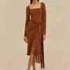 IMG_1470 - New Trend Model wearing a rust brown square‑neck wrap dress with a waist tie and fringe hem, paired with gold hoop earrings and tan sandals.