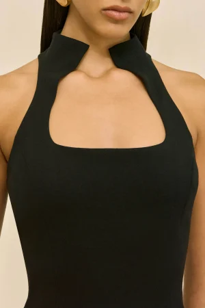Close-up of a woman wearing a black halter dress with a high collar and square neckline at the chest.
