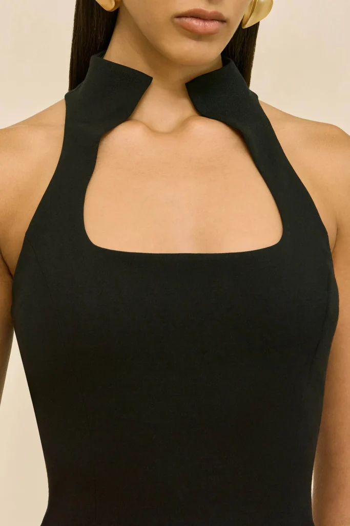 Close-up of a woman wearing a black halter dress with a high collar and square neckline at the chest.
