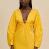 IMG_1521 - New Trend Woman wearing a bright yellow dress with a deep V-neck and twisted front detail against a beige background.