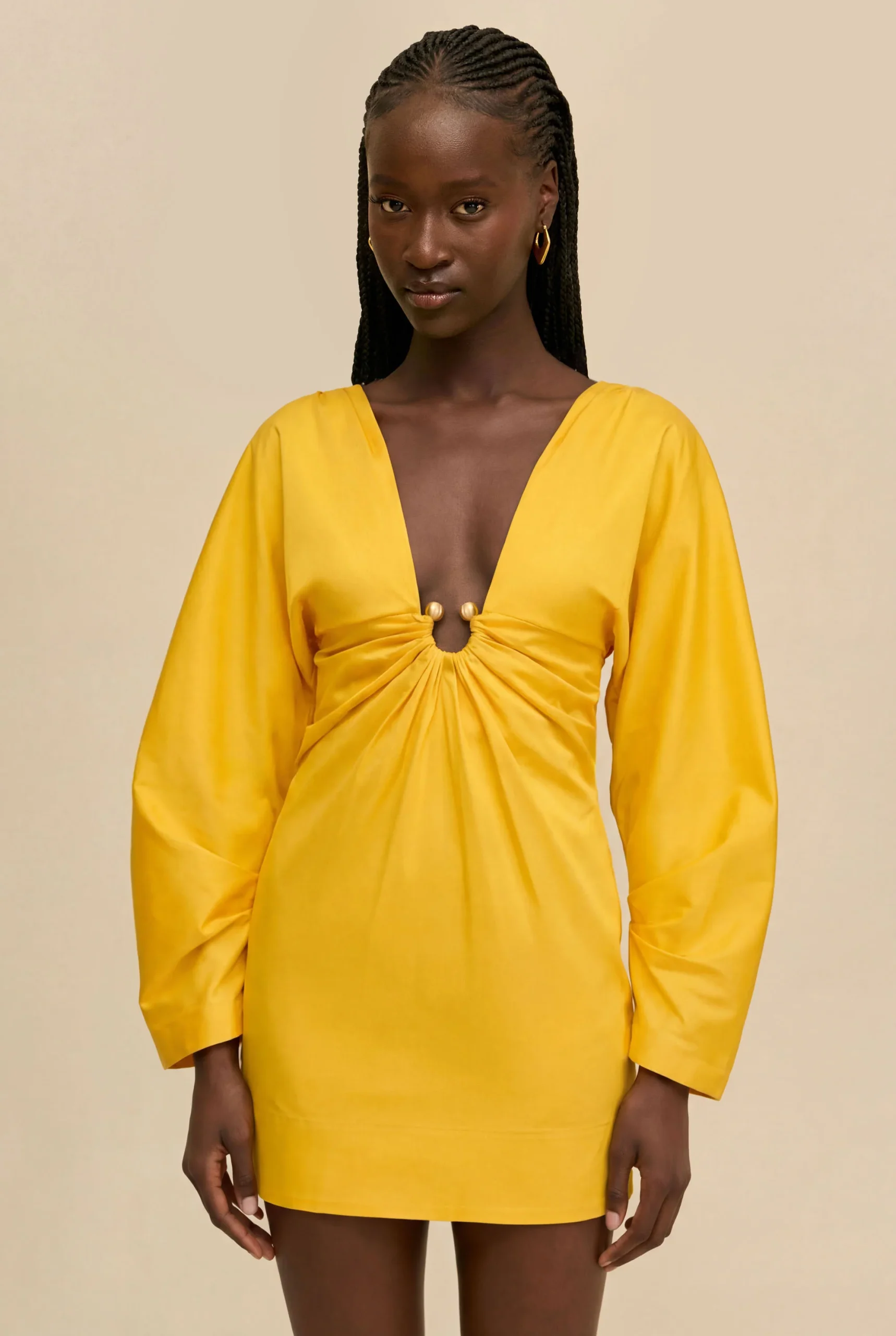 IMG_1521 - New Trend Woman wearing a bright yellow dress with a deep V-neck and twisted front detail against a beige background.