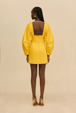 Woman standing with her back to the camera in a bright yellow dress with an open back and puff sleeves.