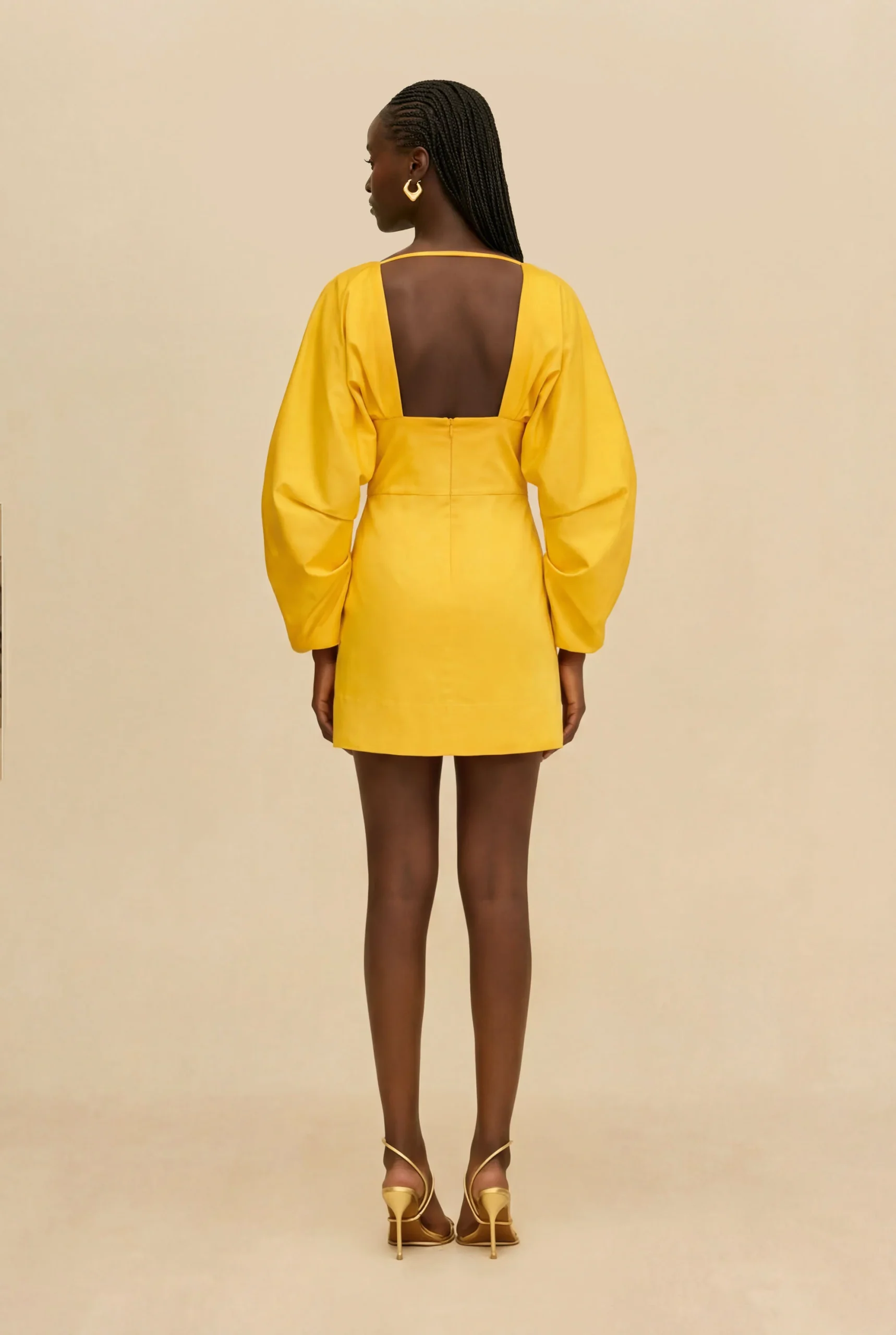 IMG_1524 - New Trend Woman standing with her back to the camera in a bright yellow dress with an open back and puff sleeves.