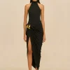 IMG_1560 - New Trend Female model wearing a black halter-neck gown with a draped skirt and gold waist accents, standing against a beige background.