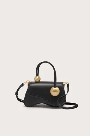 Black leather handbag with gold spherical hardware on each handle, set against a pale background.