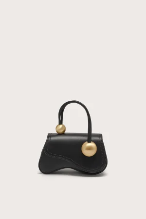 Black leather handbag with a rounded top handle and two gold spherical hardware accents on the strap, against a pale background.