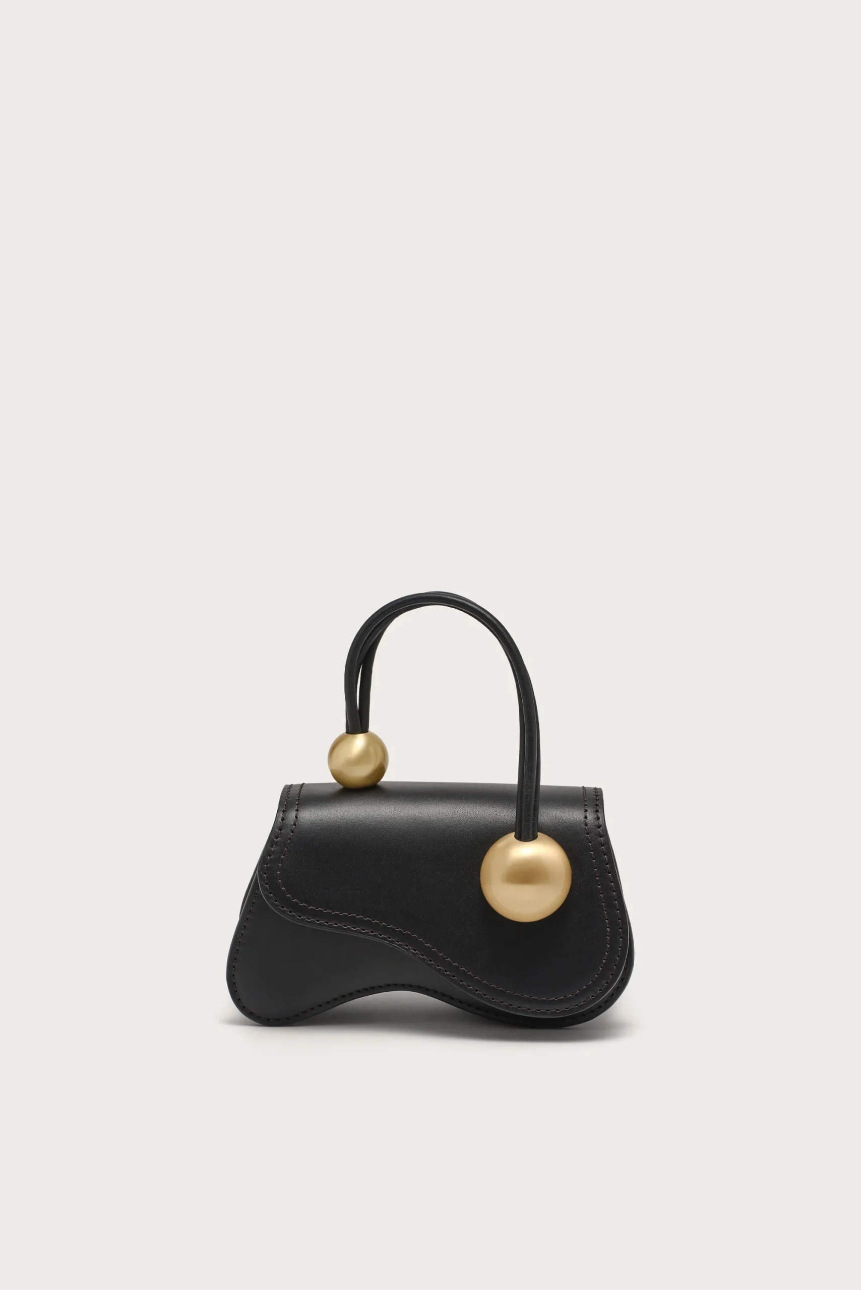 IMG_1567 - New Trend Black leather handbag with a rounded top handle and two gold spherical hardware accents on the strap, against a pale background.