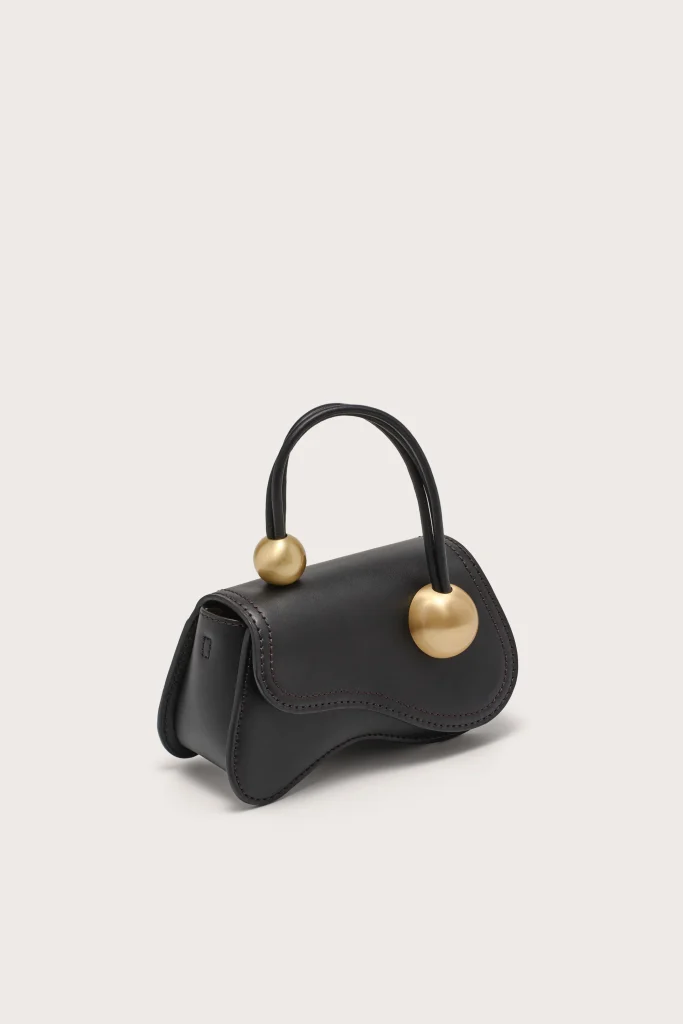 Black structured handbag with two gold spherical handles on a light background.
