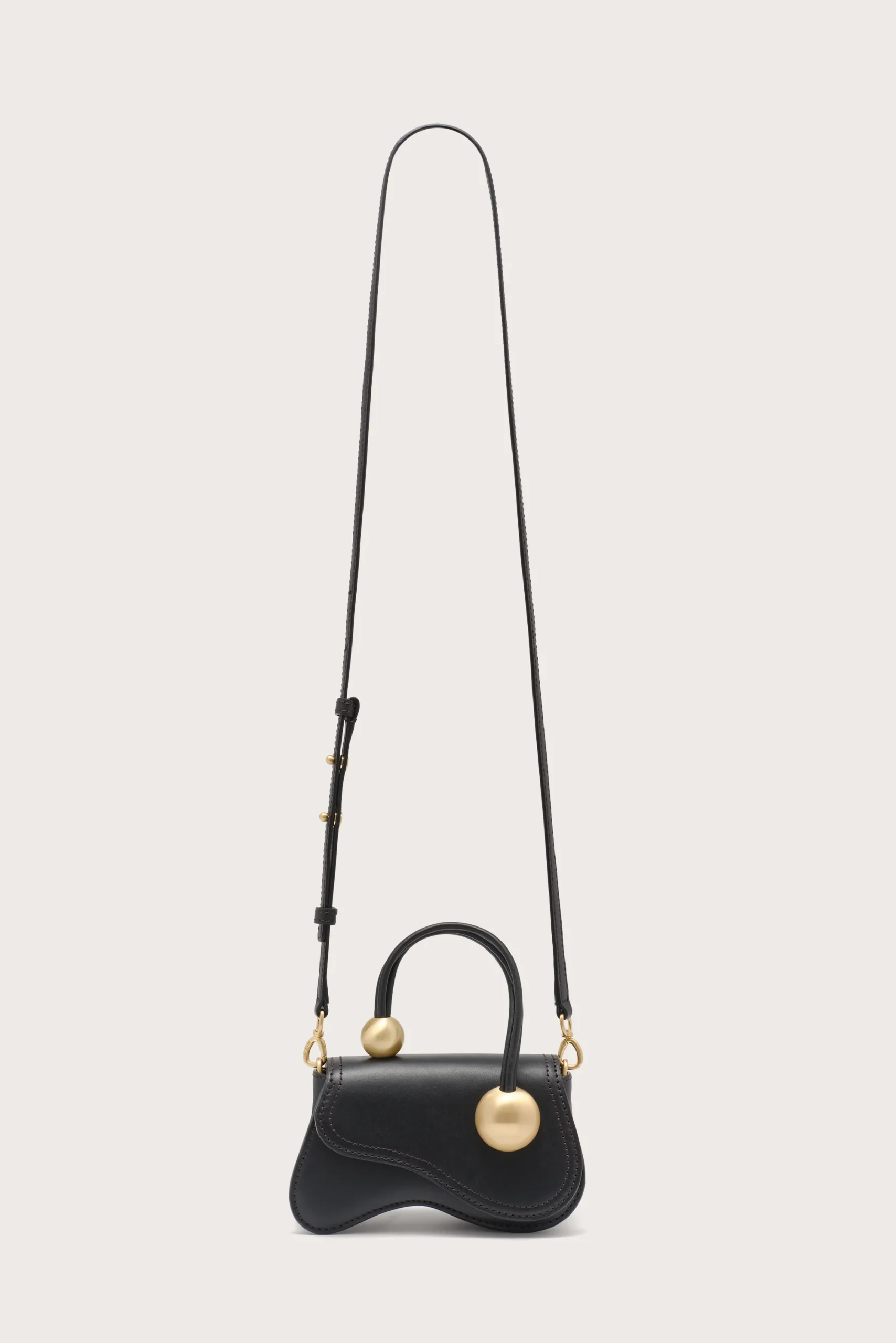 IMG_1570 - New Trend Black leather handbag with curved bottom and gold ball charms on the strap attachments, hanging from a long strap