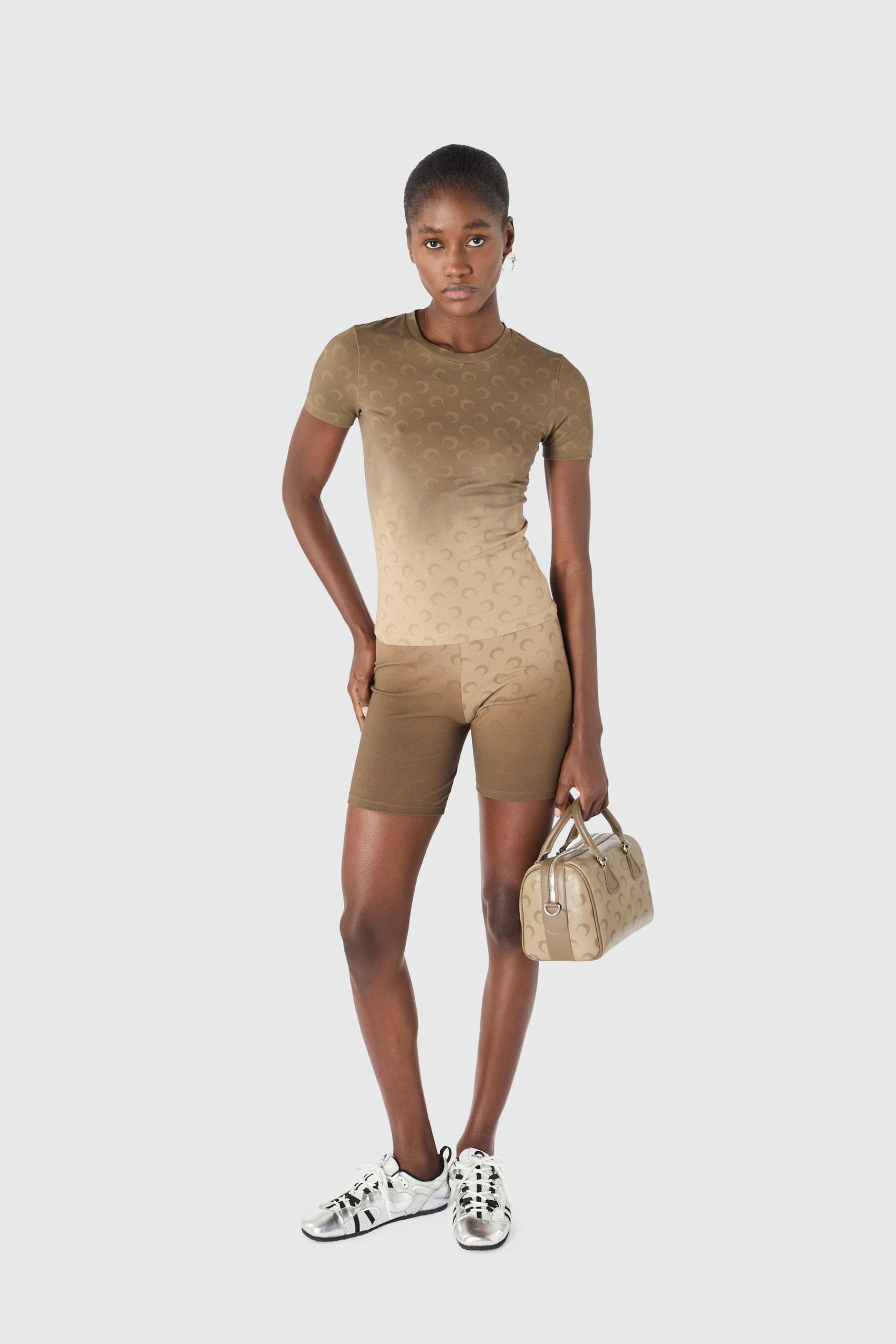 IMG_1606 - New Trend Woman in tan gradient matching athletic set (short-sleeve top and shorts) with a repeating pattern, holding a beige handbag and wearing white sneakers.
