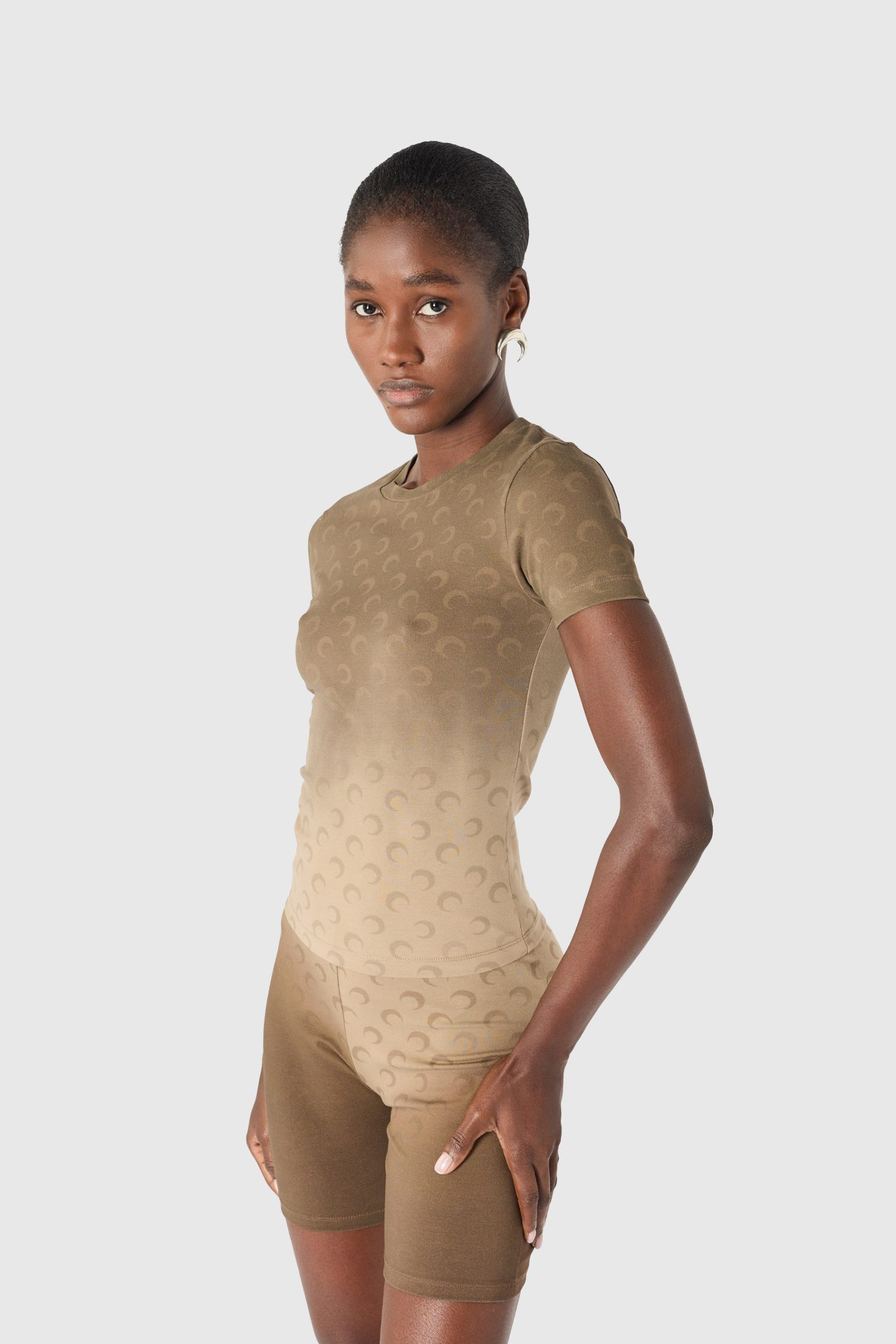 IMG_1607 - New Trend Woman modeling a beige seamless shapewear set (top and shorts) with a subtle pattern, standing in profile against a light gray backdrop.