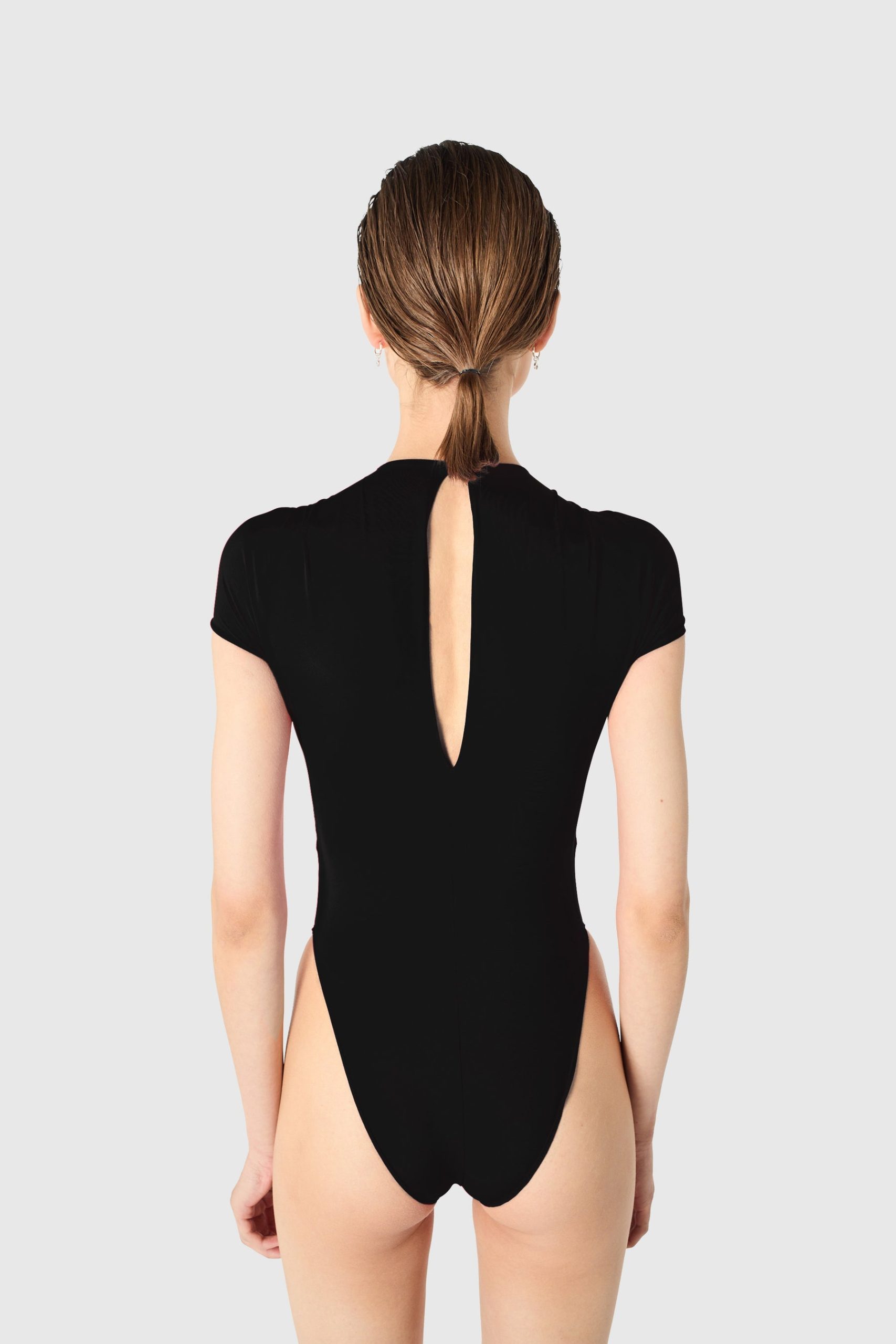IMG_1613 - New Trend Back view of a woman in a black one-piece swimsuit with a vertical back cutout and hair tied in a low ponytail
