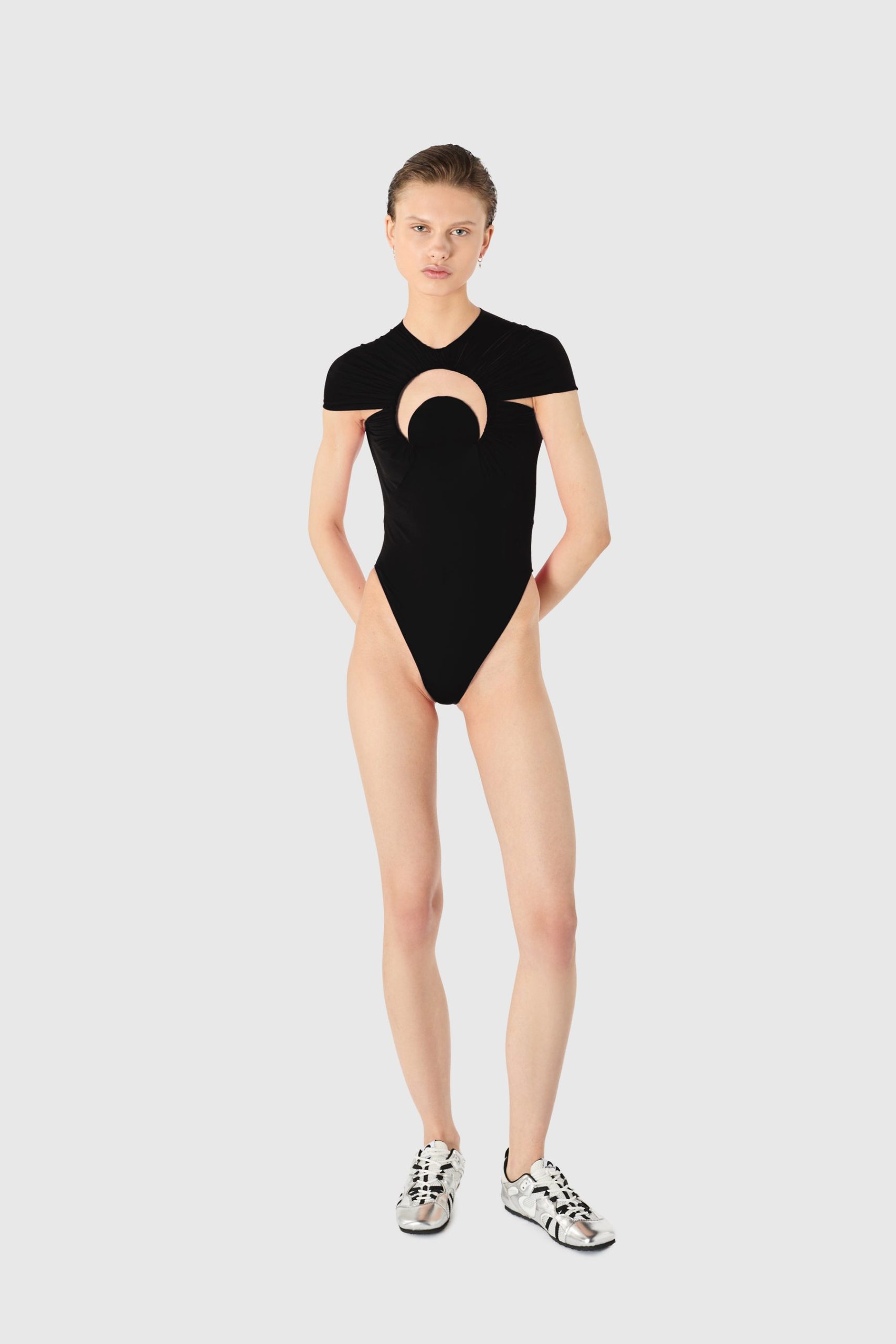 IMG_1615 - New Trend Model wearing a black one-piece bodysuit with a circular chest cutout, standing against a light gray background.