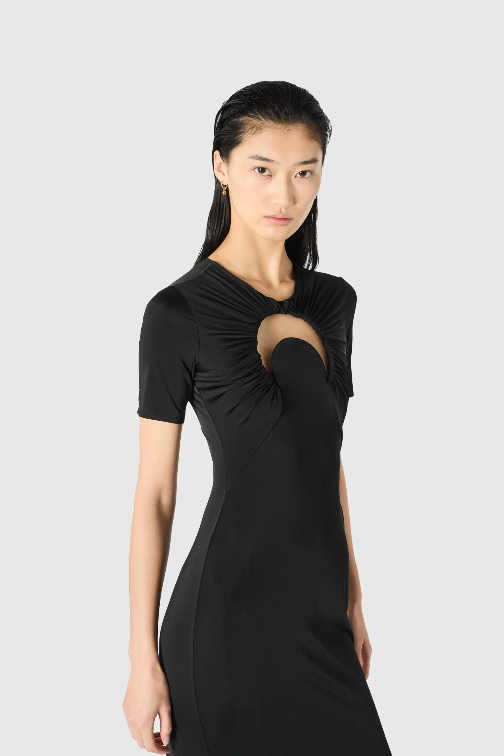 IMG_1623 - New Trend Model wearing a black dress with a ruched circular chest cutout, against a light gray background.