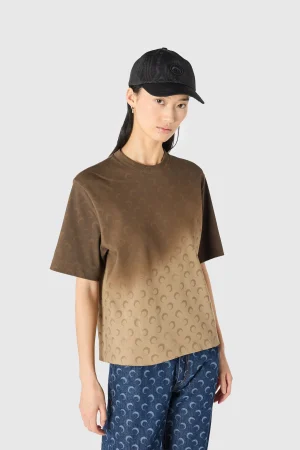Woman wearing a gradient brown T-shirt with a repeating crescent pattern and a black cap.