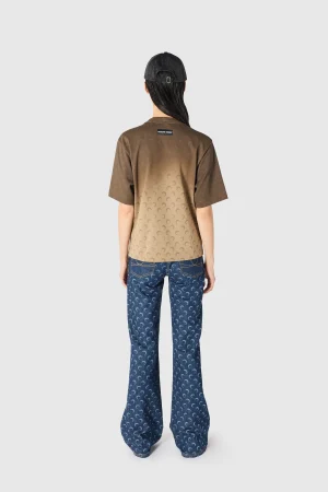 Back view of a person wearing a gradient brown short-sleeve shirt with crescent pattern, blue jeans, and a black cap.