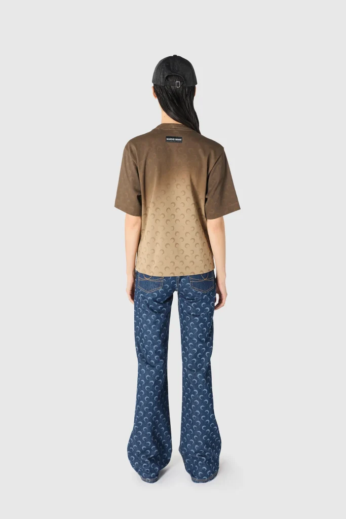 Back view of a person wearing a gradient brown short-sleeve shirt with crescent pattern, blue jeans, and a black cap.