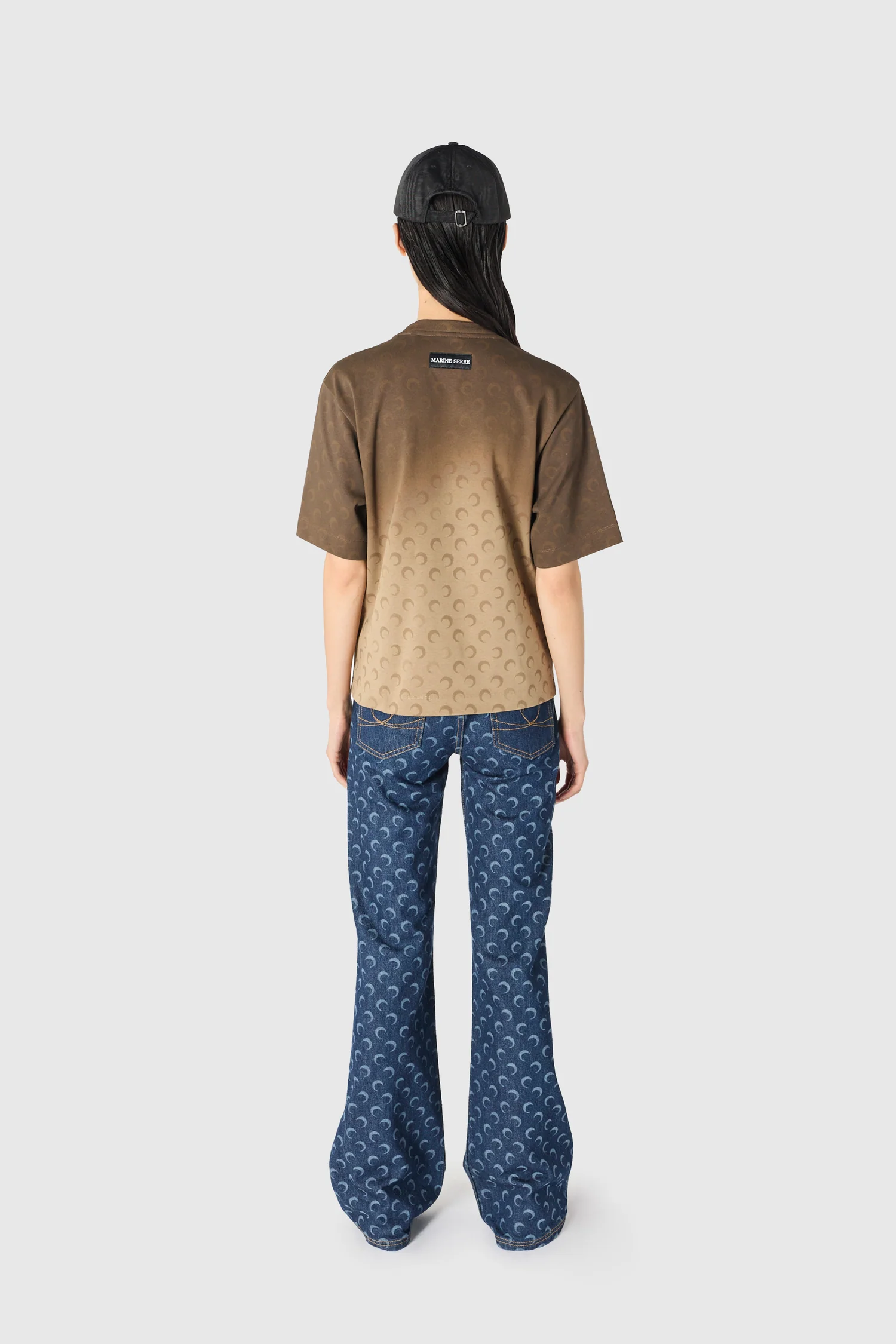 IMG_1628 - New Trend Back view of a person wearing a gradient brown short-sleeve shirt with crescent pattern, blue jeans, and a black cap.