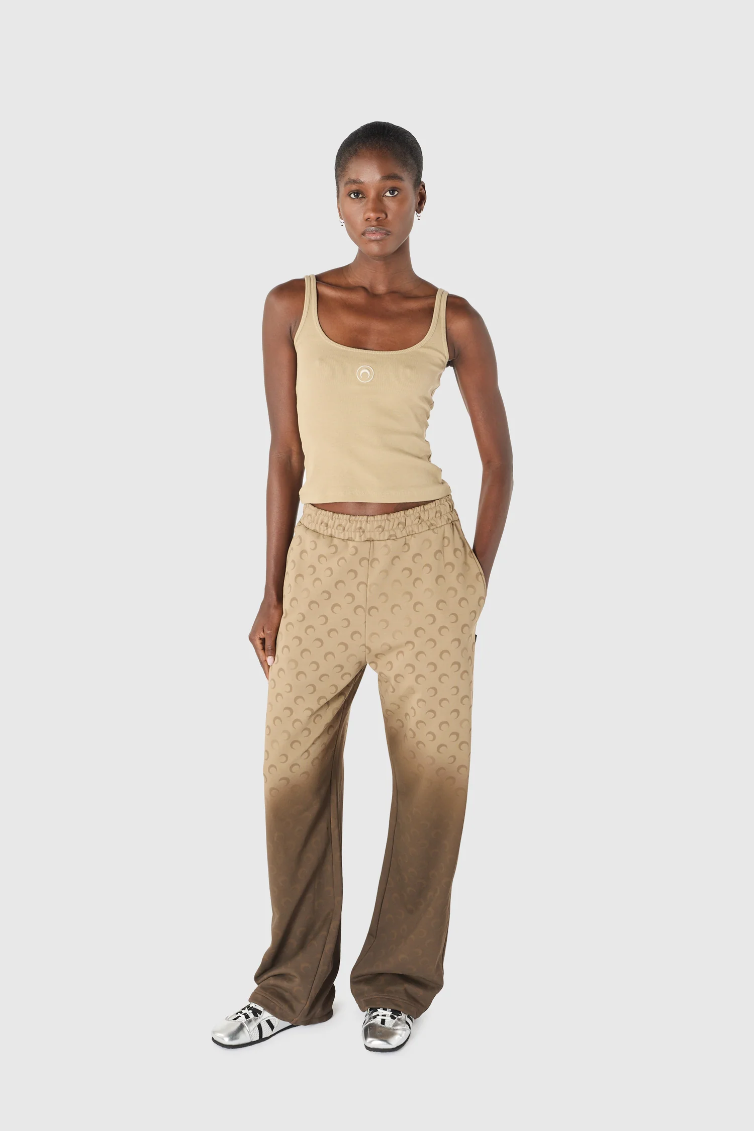 IMG_1638 - New Trend Full-body shot of a young woman wearing a beige tank top and tan patterned wide-leg pants, standing against a light gray background.